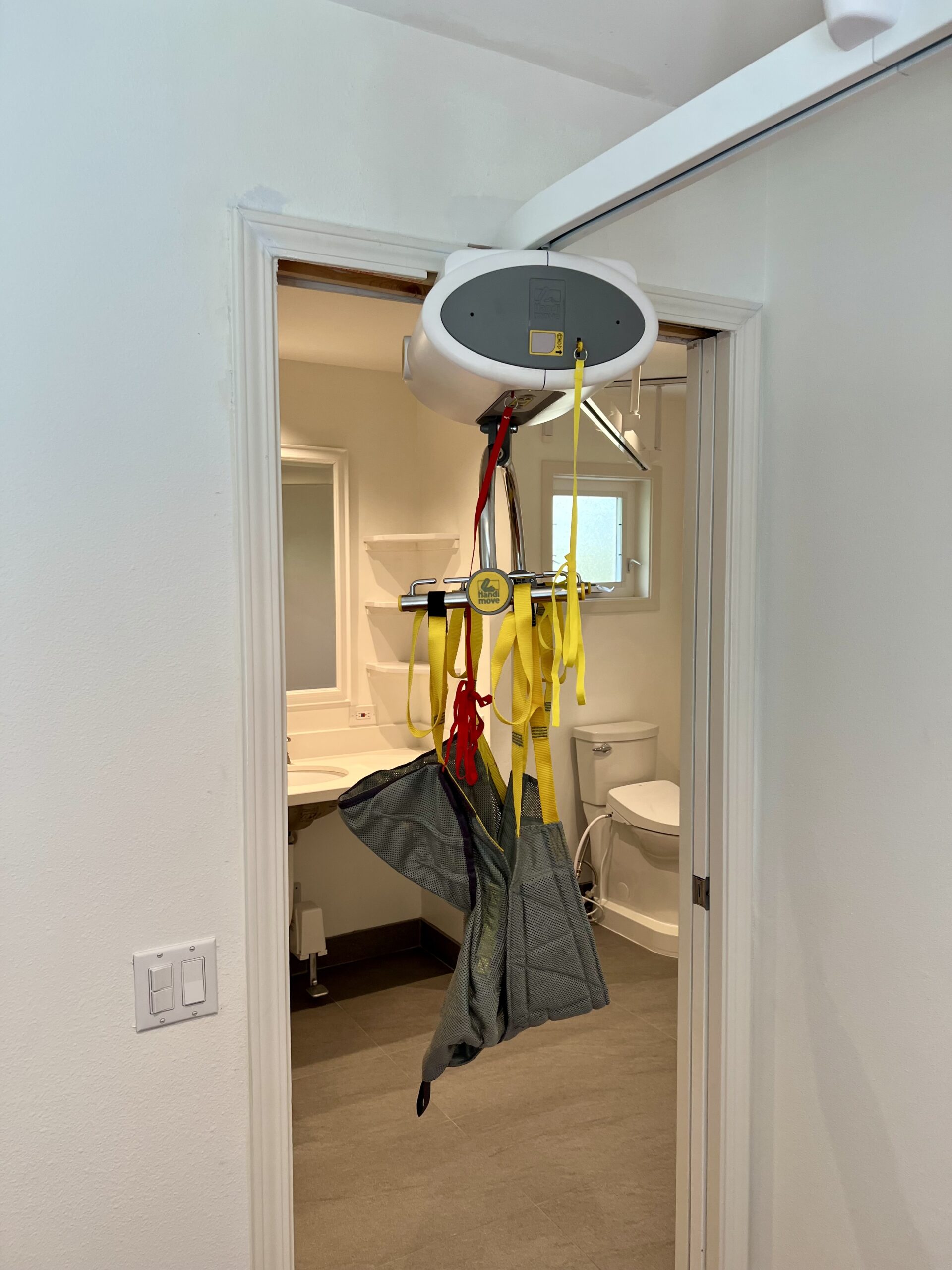 After: overhead lift track and sling through the same bathroom doorway beside the wall switches.