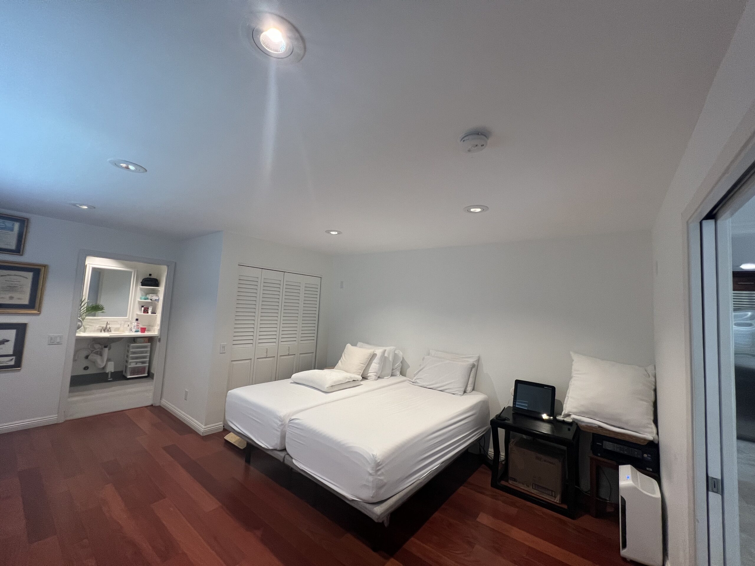 Before ceiling-lift installation: bedroom with white closet doors, an adjoining bathroom and wood floor